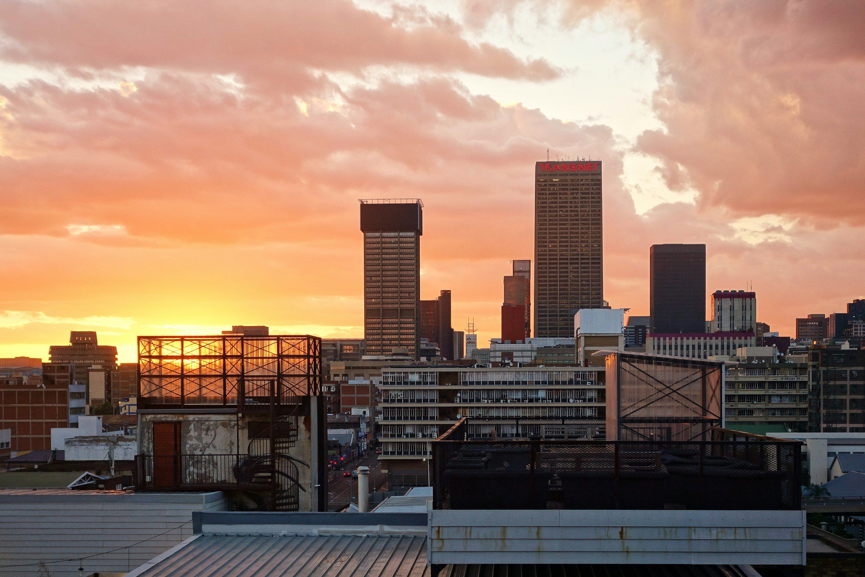 The Johannesburg skyline at dawn, its high-rises silhouetted under a cloudy orange sky