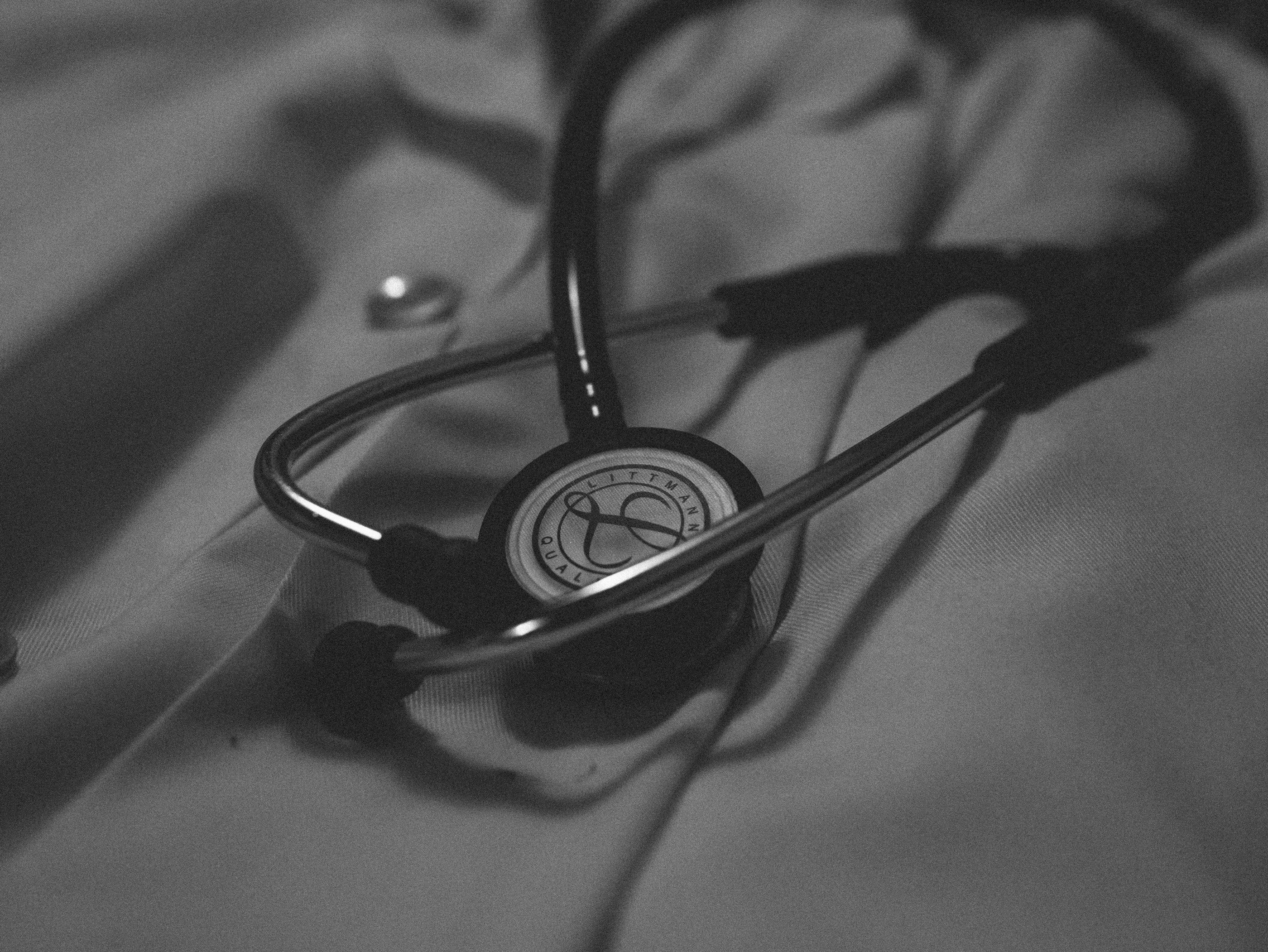 A black and white photograph of a stethoscope lying on a hospital bed